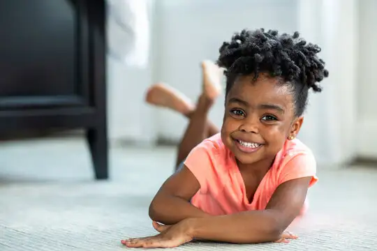 Smiling preschooler lying on a carpeted classroom floor