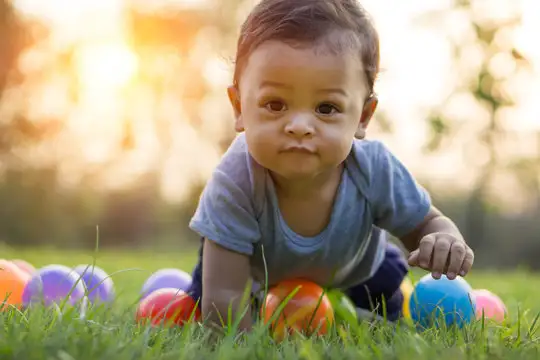 Smiling infant crawling on the grass among colorful balls