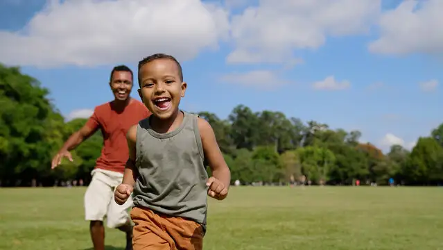 School-age child running outside with a parent in the background